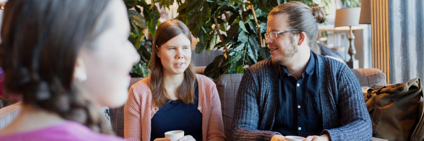 Kolme nuorta, hymyilevää aikuista kahvilassa.